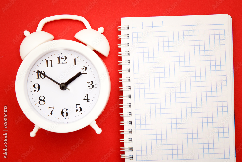 White alarm clock and notebook on red background, empty space for text. White alarm clock and notebook on red background, empty space for text.
