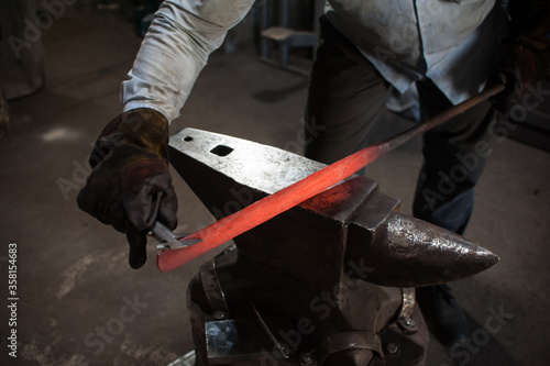 Blacksmithing. The blacksmith on the anvil measures the width of the split product. Photo of red metal close-up. The production of knive
