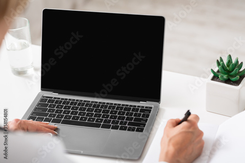 Woman doctor in white coat working at laptop and makes notes in notebook