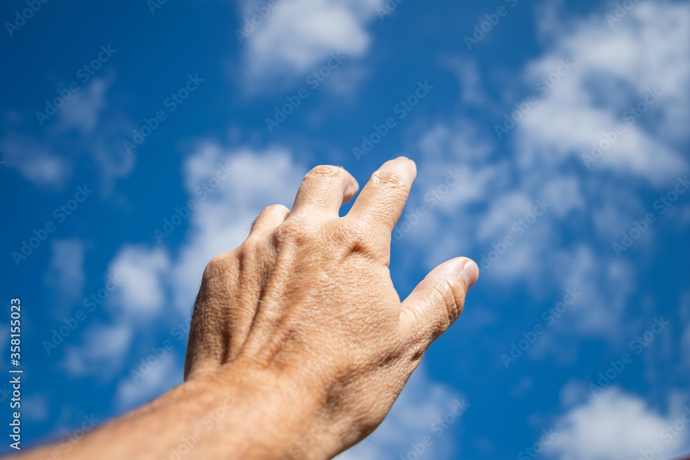 A man's hand approaching the blue sky with few clouds. symbol of faith A man's hand approaching the blue sky with few clouds. symbol of faith
