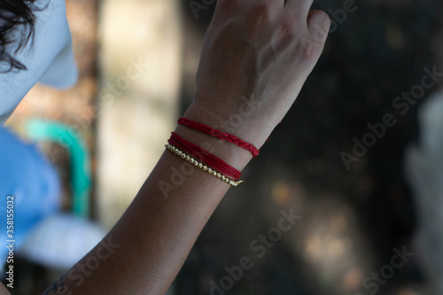 woman with white blouse and blue jenas showing her red bracelet