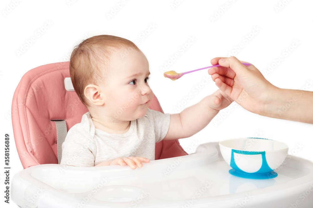 Mother feeding her cute baby girl in chair on grey background. Mother feeding her cute baby girl in chair on grey background.