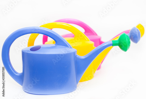 Blue, yellow and pink watering cans with shower nozzles, white background photo