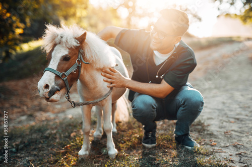 Young attractive male veterinarian enjoying with adorable little pony horse. © hedgehog94