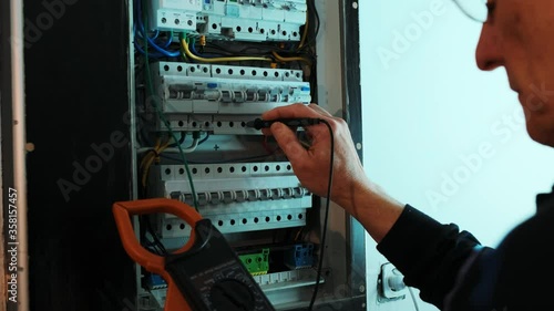 Electricians hands testing current  electric in control panel. Electrician engineer work  tester measuring  voltage and current of power electric line in electical cabinet control. photo