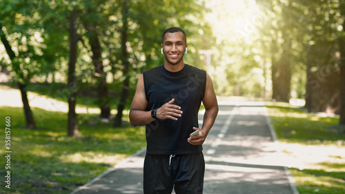 Millennial African American jogger with smartphone listening to music during his training at park