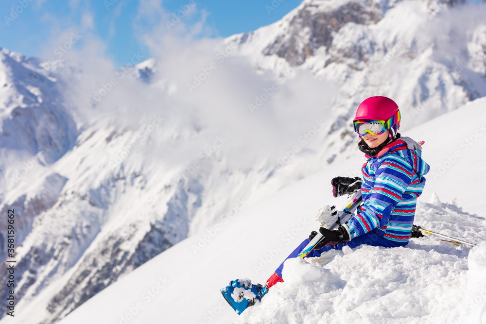 Beautiful girl in pink helmet and ski equipment sit on top of the mountain in snow observing the view Beautiful girl in pink helmet and ski equipment sit on top of the mountain in snow observing the view