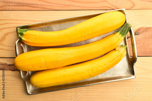 Fresh ripe, bright yellow zucchini, close-up, on a metal tray, on a white wooden table.