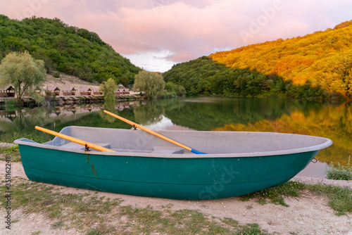 A turquoise boat stands on the shore against the lake. The lake is surrounded by hills, they grow forest. A place equipped for fishermen, fishing in a beautiful place, boat rides, romance, trip.