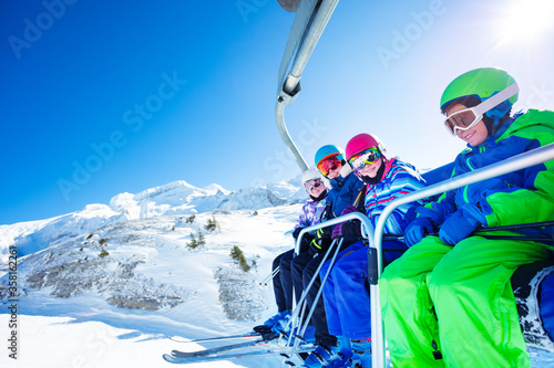 Group of four happy ski children on the chairlift over mountain top peak on perfect summer day