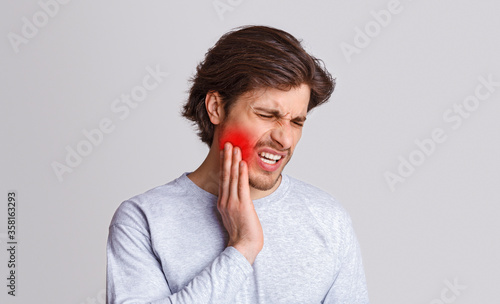 Endure pain. Sad man suffers from pain in his teeth and presses hand to red spot