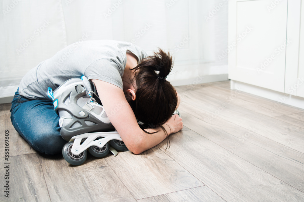 Sad woman with dark hair is sitting on floor in room with her arms around roller skates. Faceless shot. Quarantine time. Self-isolation. Activity at home Sad woman with dark hair is sitting on floor in room with her arms around roller skates. Faceless shot. Quarantine time. Self-isolation. Activity at home