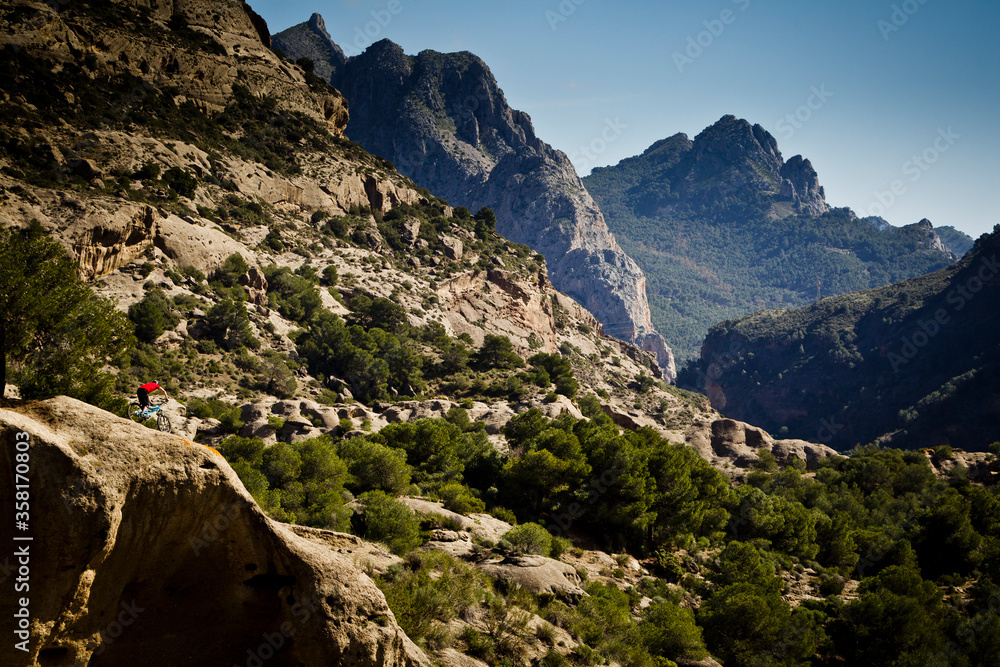 EL CHORRO, MALAGA, SPAIN. A mountain biker riding through dramatic rocky wilderness with high peaks behind.