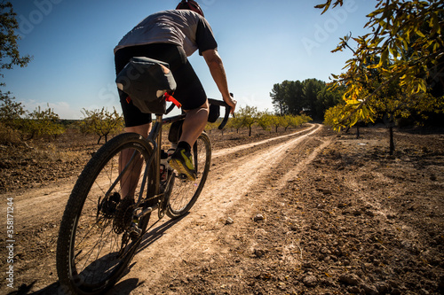 EL CHORRO, SPAIN. A man riding a 'gravel bike' along a smooth dirt road though a plantation of almond trees.
