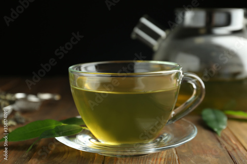 Cup of aromatic green tea and leaves on wooden table