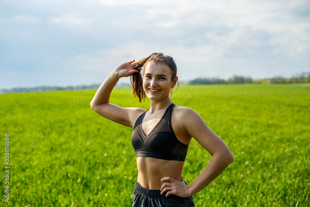 Girl athlete does warm-up outdoors, exercises for muscles. Young woman go in for sports, healthy lifestyle, athletic body. She is in sportswear, black top and shorts. Sport concept.