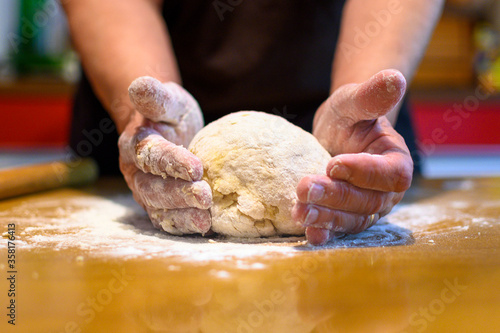 Skillful hands kneading dough for bread on kitchen table.