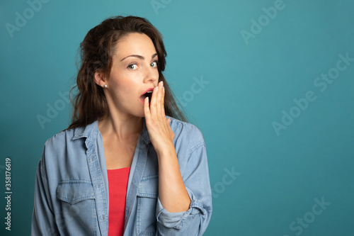 young woman putting her hand in front of mouth on blue background
