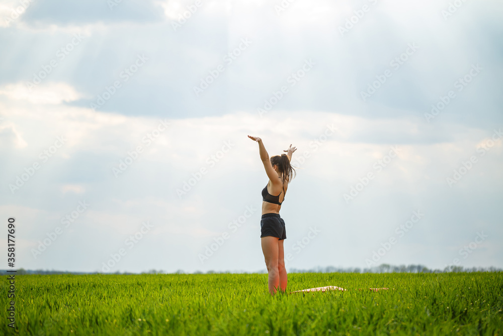 Attractive girl athlete does warm-up outdoors, exercises for muscles. Young woman go in for sports, healthy lifestyle, athletic body. She is in sportswear, black top and shorts Attractive girl athlete does warm-up outdoors, exercises for muscles. Young woman go in for sports, healthy lifestyle, athletic body. She is in sportswear, black top and shorts