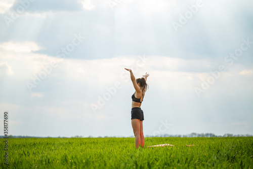 Attractive girl athlete does warm-up outdoors, exercises for muscles. Young woman go in for sports, healthy lifestyle, athletic body. She is in sportswear, black top and shorts