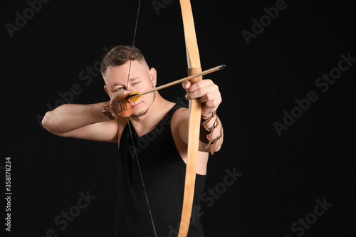 Handsome male archer with bow on dark background