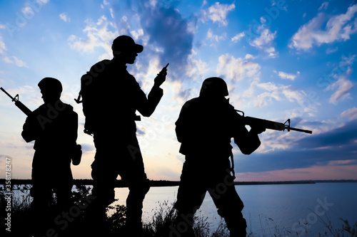 Obraz na plátně Silhouettes of soldiers with assault rifles and portable radio transmitter patrolling outdoors