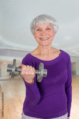 Happy charming beautiful elderly woman is doing exercise with a dumbbell. Exercising gymnastics for health in the fitness room. Sports training