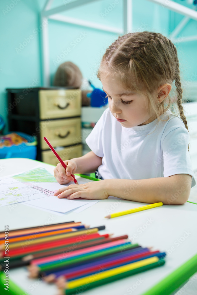 Adorable toddler girl drawing with pencils at home sitting at the table. Creative child sitting in a room learning to draw. Toddler girl doing homework at home. Adorable toddler girl drawing with pencils at home sitting at the table. Creative child sitting in a room learning to draw. Toddler girl doing homework at home.