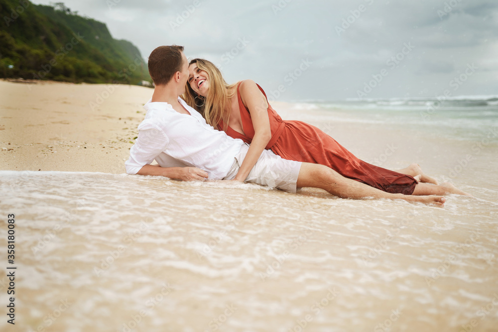 Girl and guy lie on the beach of the ocean on the waves against the backdrop of the mountains
