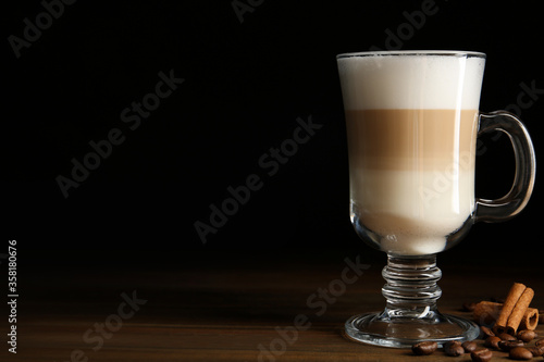 Delicious latte macchiato, cinnamon and coffee beans on wooden table against black background, space for text © New Africa