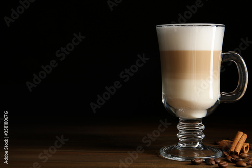 Delicious latte macchiato, cinnamon and coffee beans on wooden table against black background, space for text