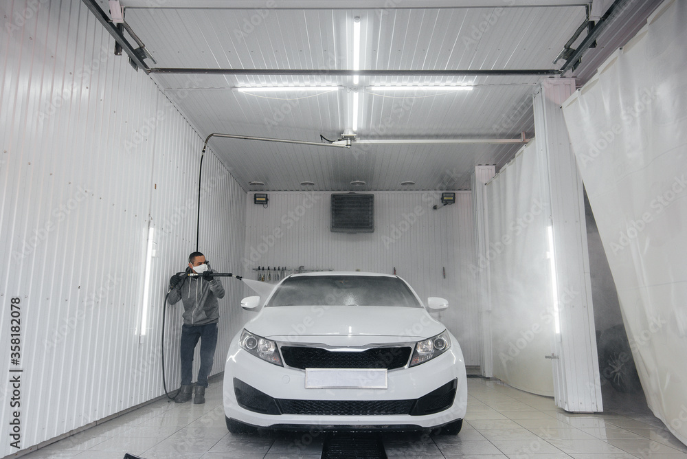 Modern washing with foam and high-pressure water of a white car. Car wash