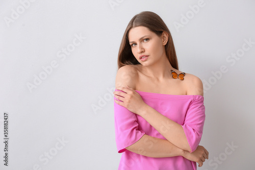 Beautiful young woman with butterfly on light background