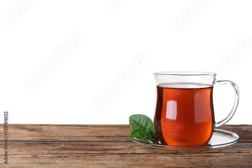 Glass cup of aromatic black tea and green leaves on wooden table against white background. Space for text