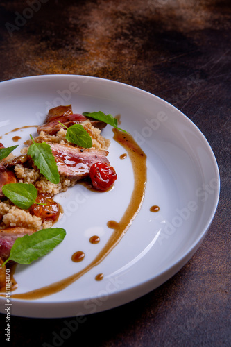 A quinoa, teriyaki sauce and confit tomatoes on a white plate against a dark background. Master class in the kitchen. The process of cooking. Dish from the restaurant menu. European cuisine. Close-up