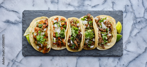 Φωτογραφία row of mexican street tacos on slate with carne asada and al pastor in corn tort