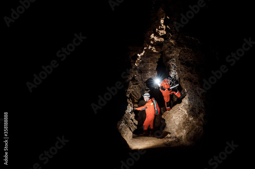 Two men, strong physique, explore the cave. Men dressed in special clothes to pass through the cave and stopped, looking at the map photo