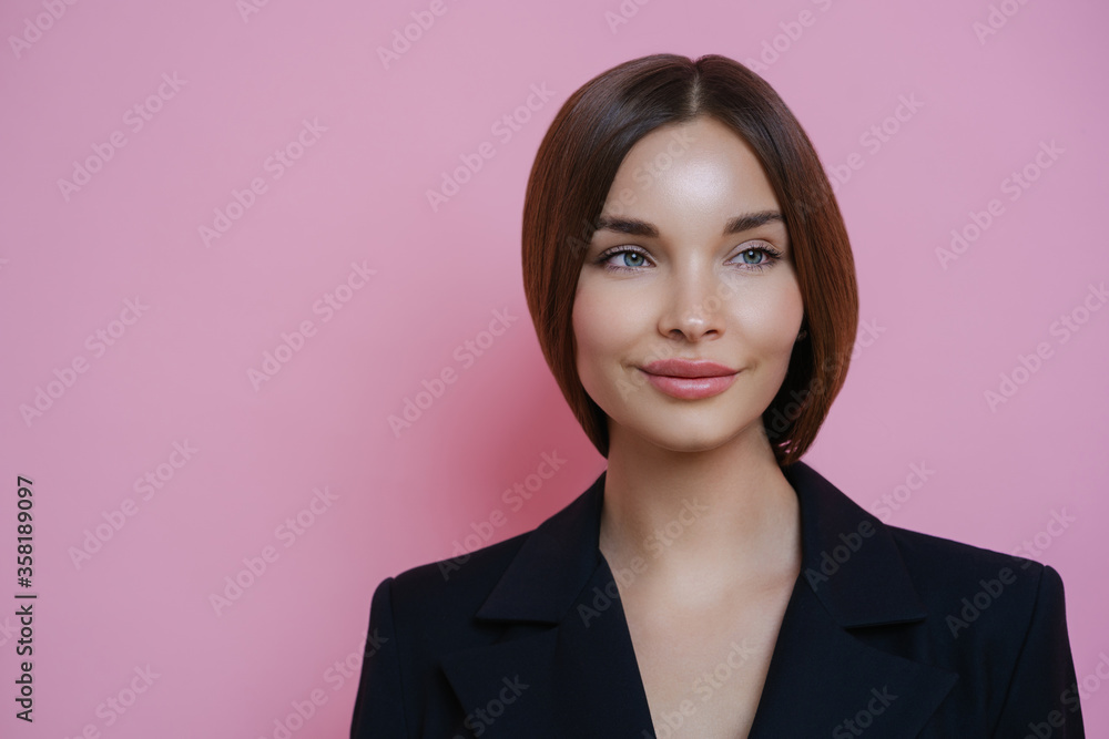 Beautiful businesswoman looks aside with dreamy expression, thinks about something pleasant during break after work, wears black clothing, isolated on pink background, empty space for your information Beautiful businesswoman looks aside with dreamy expression, thinks about something pleasant during break after work, wears black clothing, isolated on pink background, empty space for your information