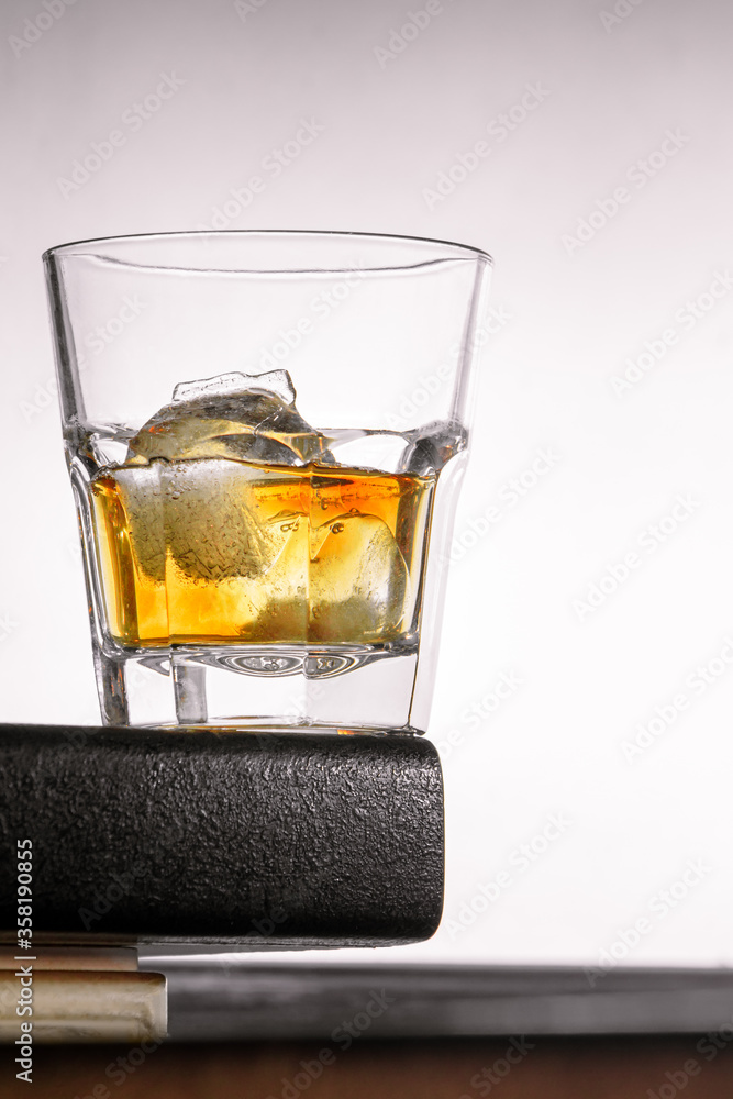 a glass of whiskey with ice stands on the corner of the bar counter on a light gray background. close up, bot view, copy space. vertical orientation a glass of whiskey with ice stands on the corner of the bar counter on a light gray background. close up, bot view, copy space. vertical orientation