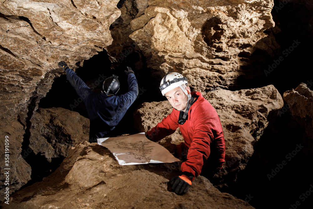 Two men, strong physique, explore the cave. Men dressed in special clothes to pass through the cave and stopped, looking at the map Two men, strong physique, explore the cave. Men dressed in special clothes to pass through the cave and stopped, looking at the map