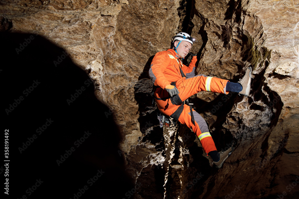 Obraz premium Speleologist descend by the rope in the deep vertical cave tunnel. Cave man hanging over abyss. View from the top og the tunnel.