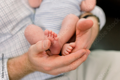 Newborn Baby Feet in Father's Hands. Dad is wearing khaki pants and a plaid shirt. Newborn photography session. 