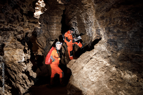 Two men, strong physique, explore the cave. Men dressed in special clothes to pass through the cave and stopped, looking at the map photo