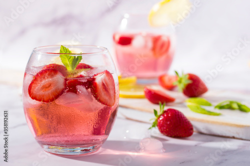 Cold pink strawberry flavoured jin and tonic garnished with fresh fruits and mint leaves.