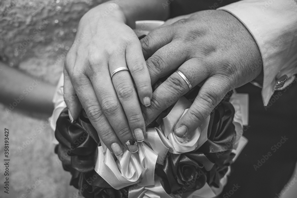 Bride and groom's hands on top of the bouquet with wedding rings