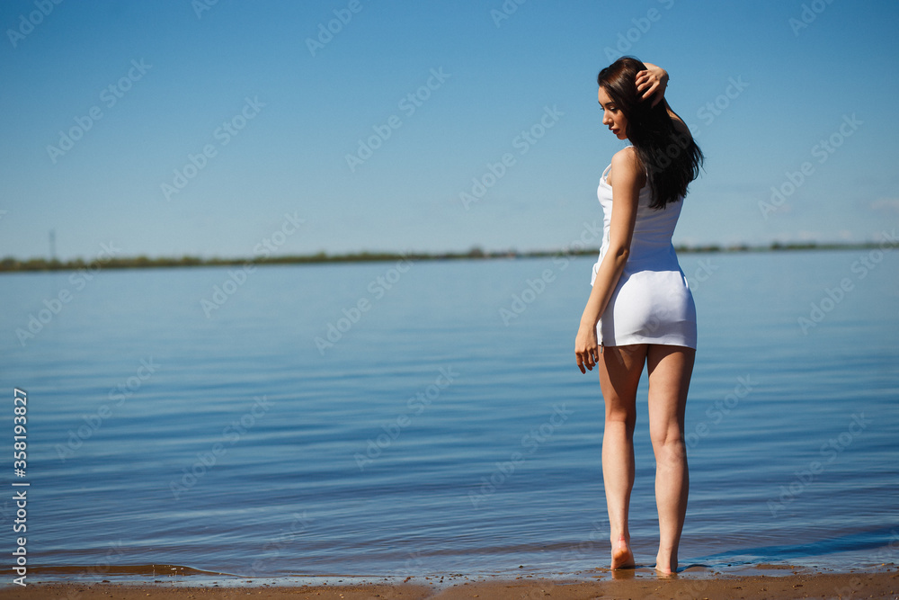 Naklejka premium Young sexy lady in the white dress standing in the warm water.