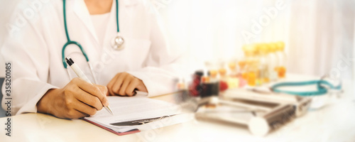 Close-up hands Female doctor in a white coat and headphones on duty  recording clipboard  taking medication on the hospital desk 