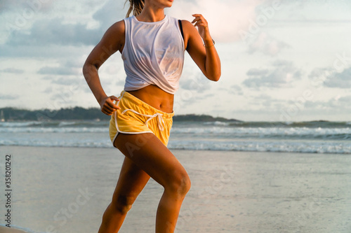 Young fit woman running jogging on the beach. Outdoor fitness and work out alone. Bright sports outfit. Ocean background. Copy space