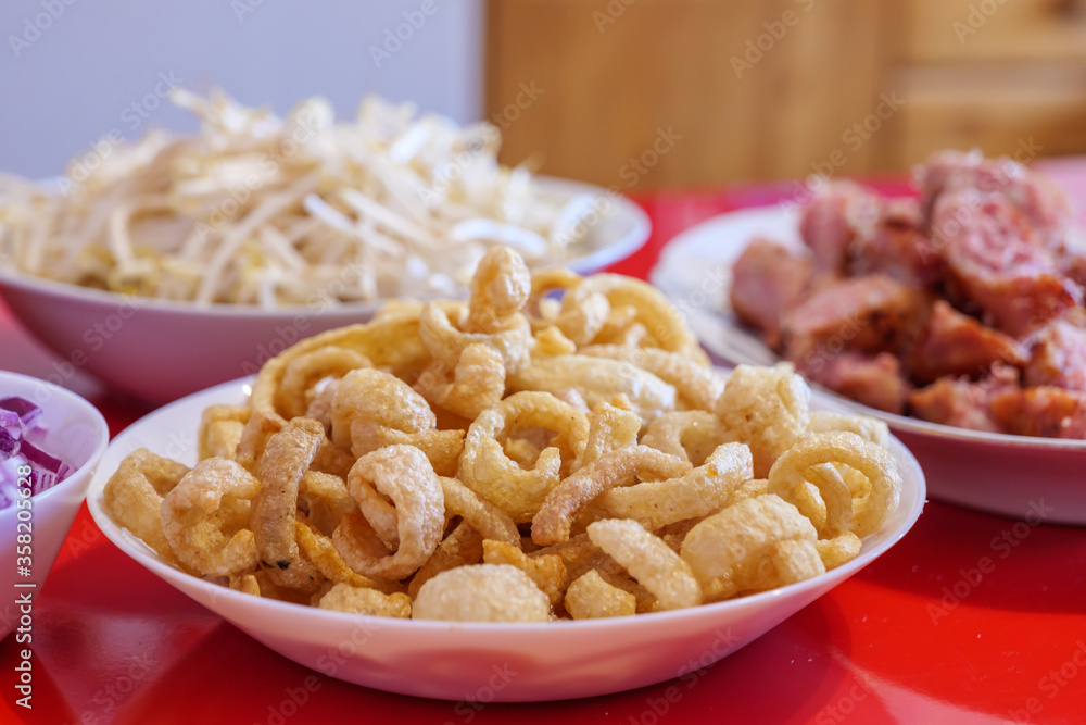 Pile of deep fried or bake pork snack, pork rind, pork scratching or pork crackling on white dish and blur background of North East Thai Sausage. Pile of deep fried or bake pork snack, pork rind, pork scratching or pork crackling on white dish and blur background of North East Thai Sausage.