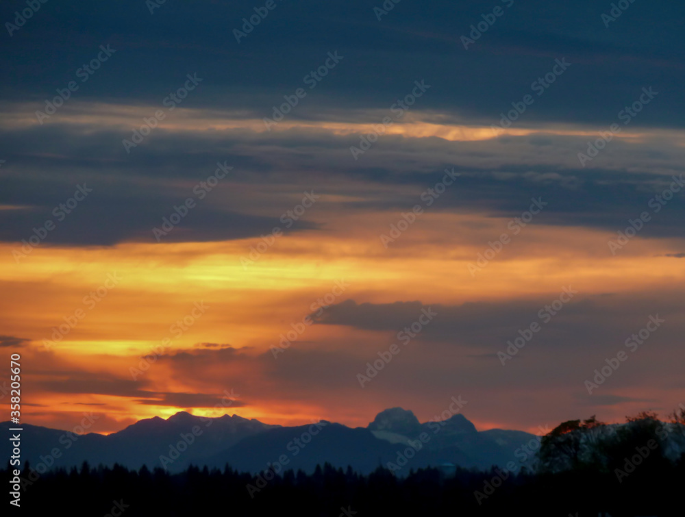 Silhouette of Pacific Northwest Cascade Range and evergreen forest with dark and orange sky in the twilight hours.